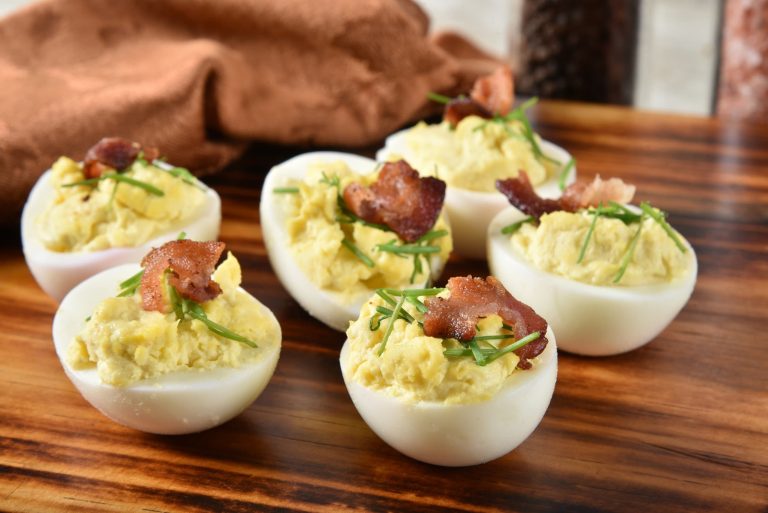 oeufs farcis à la diable avec du cheddar et du bacon servis sur une planche de bois