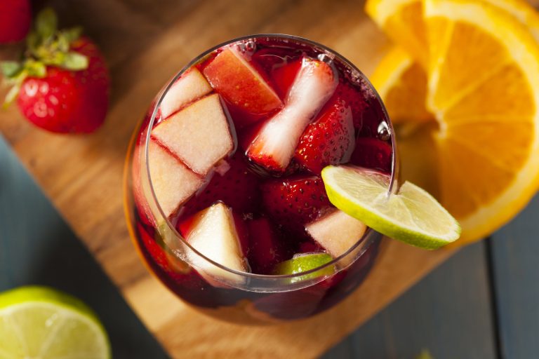 Sangria au vin rouge remplie de morceaux de fruits dans un verre et sur une planche à découper vue de haut