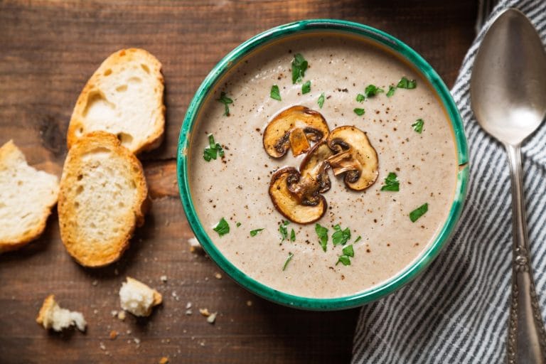 Crème de champignons cuisinée dans l'autocuiseur Instant Pot ou cocotte minute et servie dans un bol vert avec du pain. Des tranches de champignons sautés et du persil frais décore le plat.