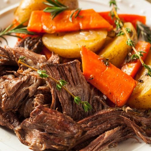 Rôti de palette au four tendre et juteux dans une assiette avec carottes et patates et branches de thym.