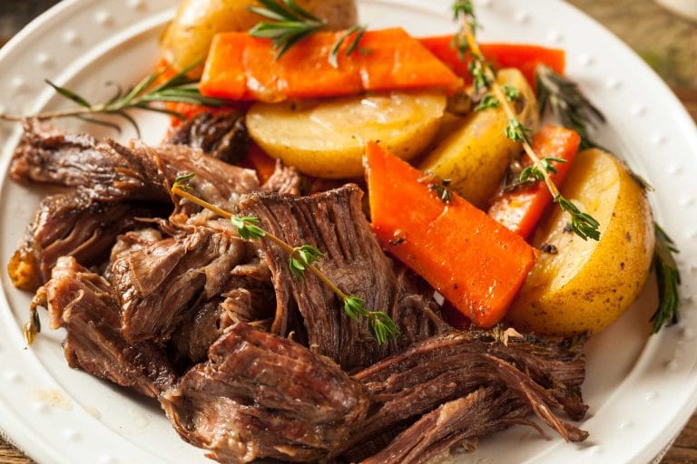 Rôti de palette au four tendre et juteux dans une assiette avec carottes et patates et branches de thym.