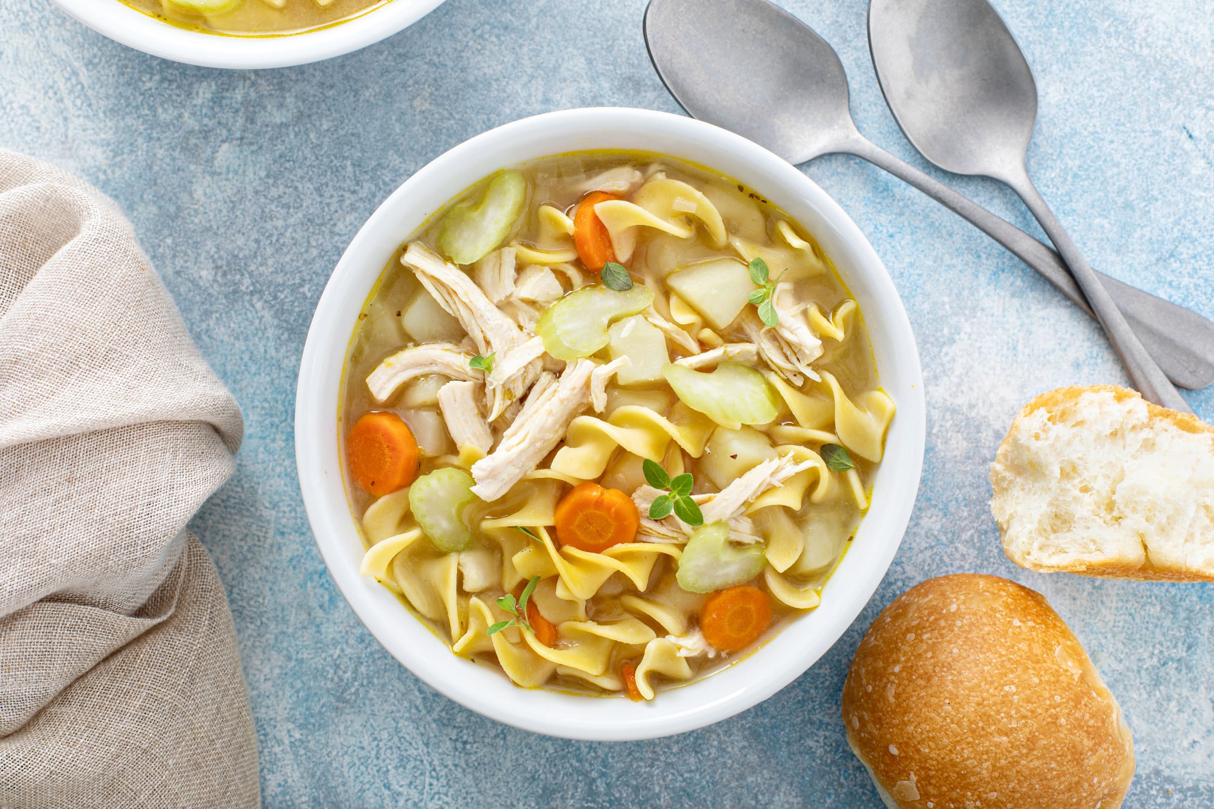 Soupe au poulet au aux nouilles avec carottes, céleri en morceaux servie dans un bol blanc avec du pain.