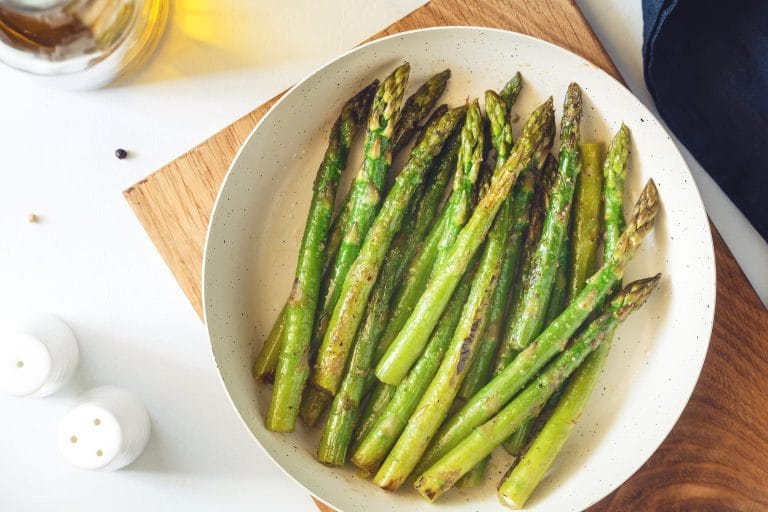 Asperges rôties au Air Fryer servies dans une assiette blanche sur une planche de bois avec sel et poivre