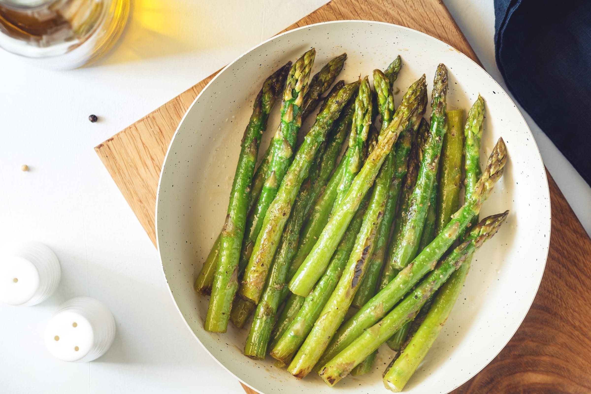Asperges rôties au Air Fryer servies dans une assiette blanche sur une planche de bois avec sel et poivre