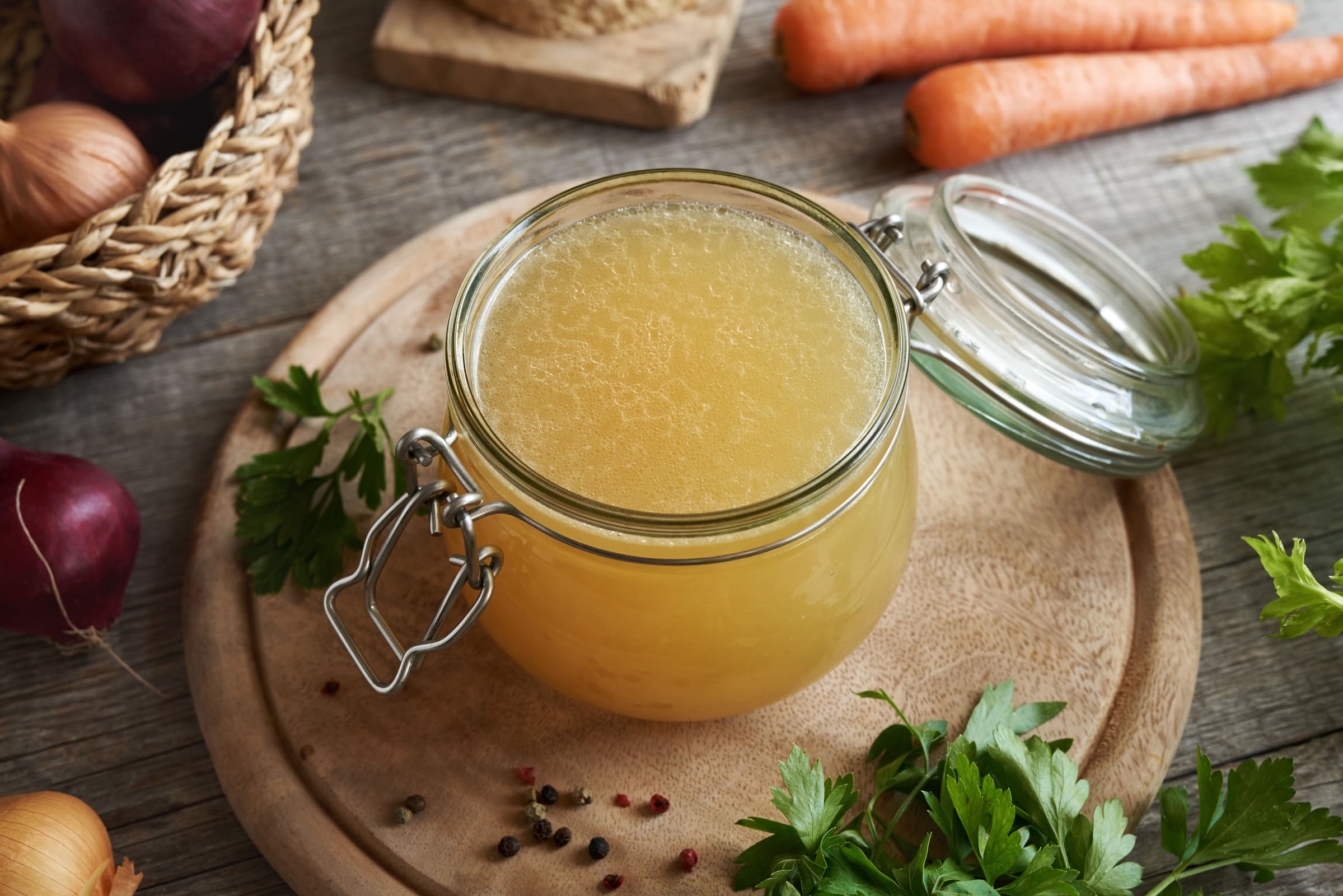 Bouillon de poulet maison fait à l'autocuiseur Instant Pot versé dand un pot mason sur une planche de bois avec des légumes autour.