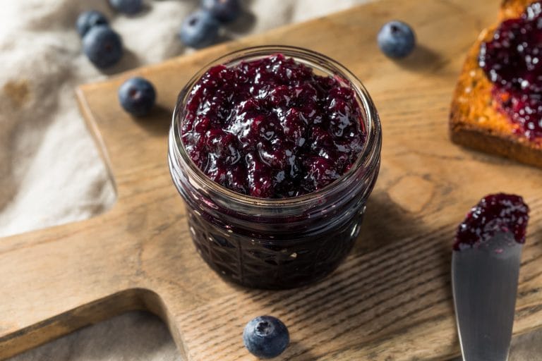 Pot mason rempli de confiture de bleuets déposé sur une planche de bois.