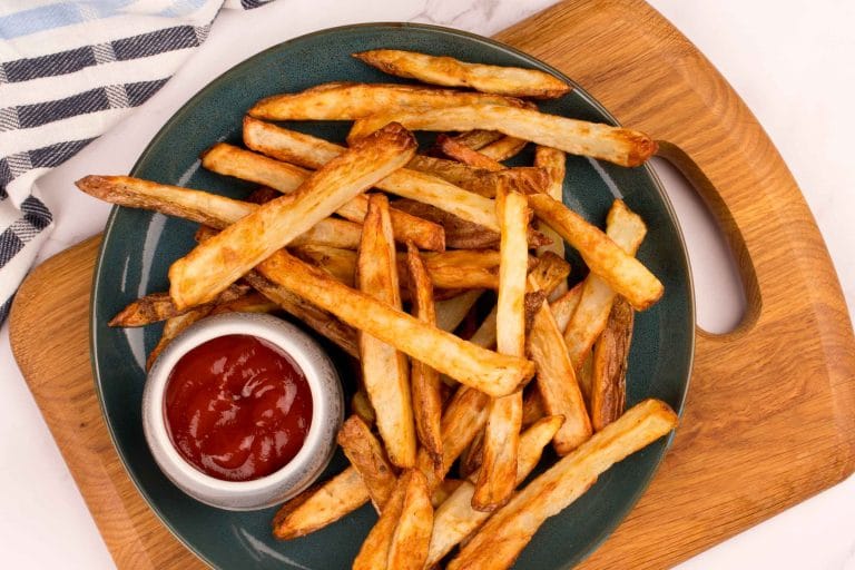 Frites maison à la friteuse à air dans une assiette verte et servies avec un petit bol de ketchup.