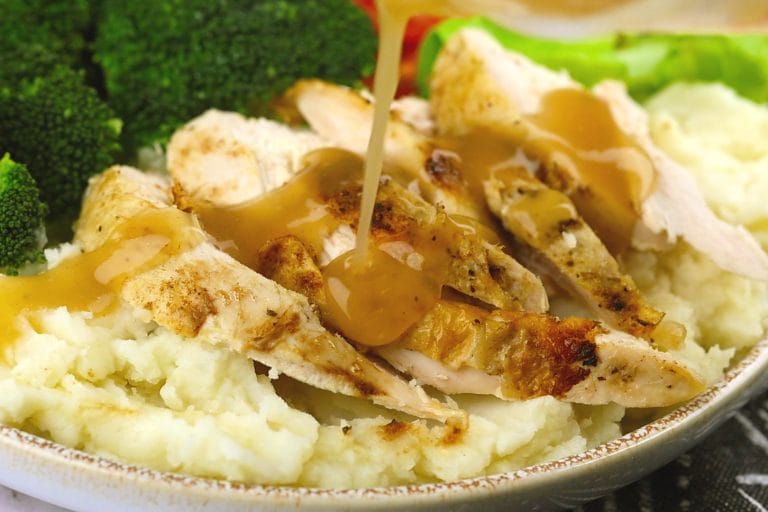 Tranches de poitrine de poulet rôti cuit à l'Instant Pot sur lit de pommes de terre en purée, arrosé de sa sauce et accompagné de brocoli.