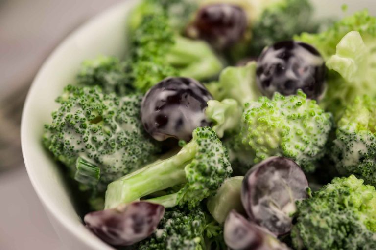 Salade avec bouquets de brocoli et des morceaux de raisins frais avec vinaigrette crémeuse servie dans un bol blanc