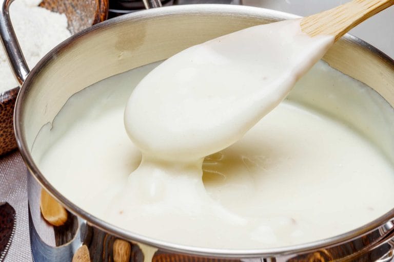 Sauce blanche béchamel qui cuit dans une casserole et une cuillère de bois remplie de sauce