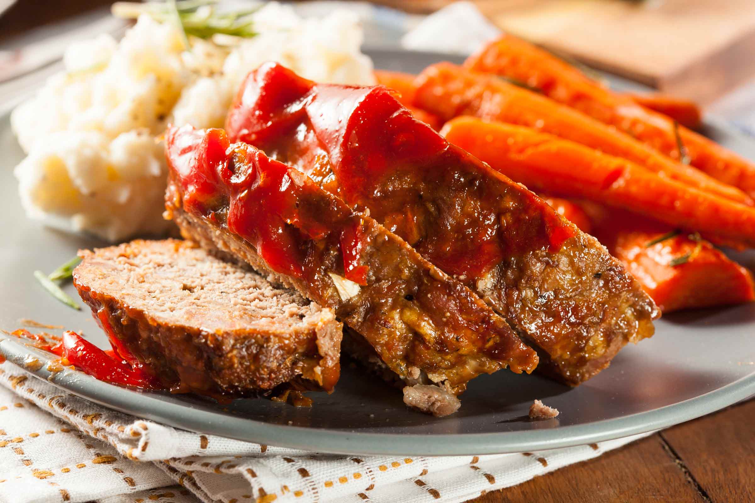 pain de viande avec sauce au ketchup et cassonade, purée de pommes de terre et carottes sur une assiette grise
