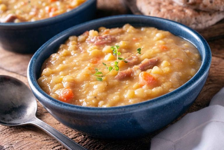 Soupe aux pois au jambon et au sirop d'érable servie dans un bol bleu et garni d'une tige de thym