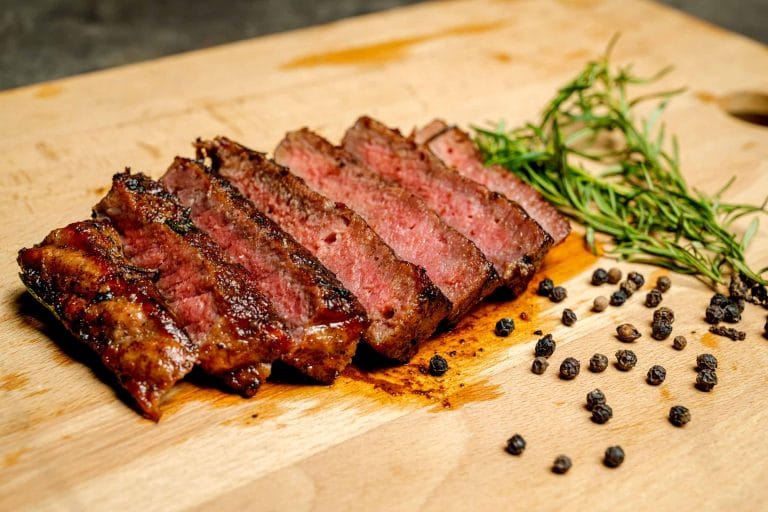 Steak avec marinade grillé et juteuse tranché et placé sur une planche de bois décoré avec brin de romarin et poivre noir