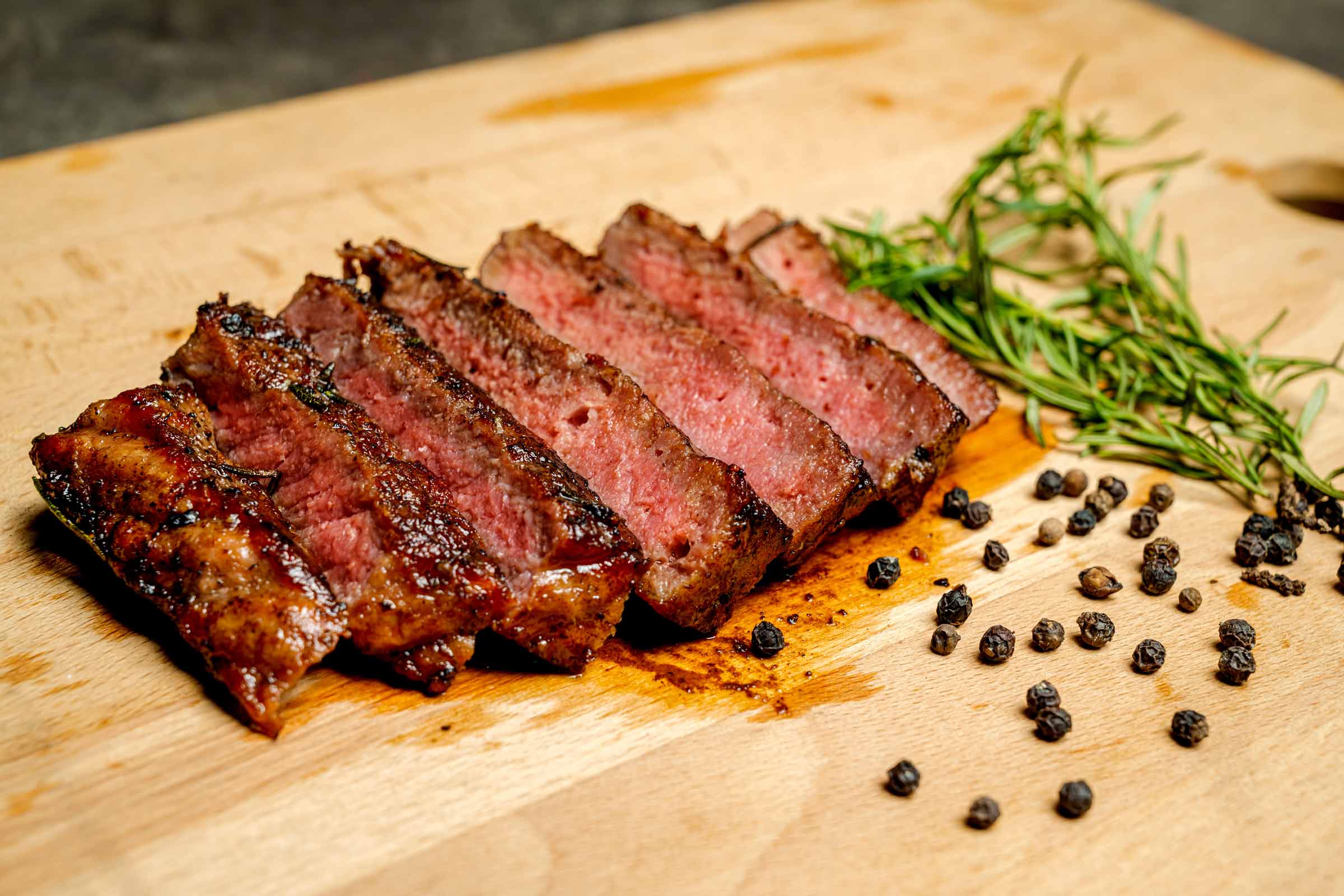 Steak avec marinade grillé et juteuse tranché et placé sur une planche de bois décoré avec brin de romarin et poivre noir