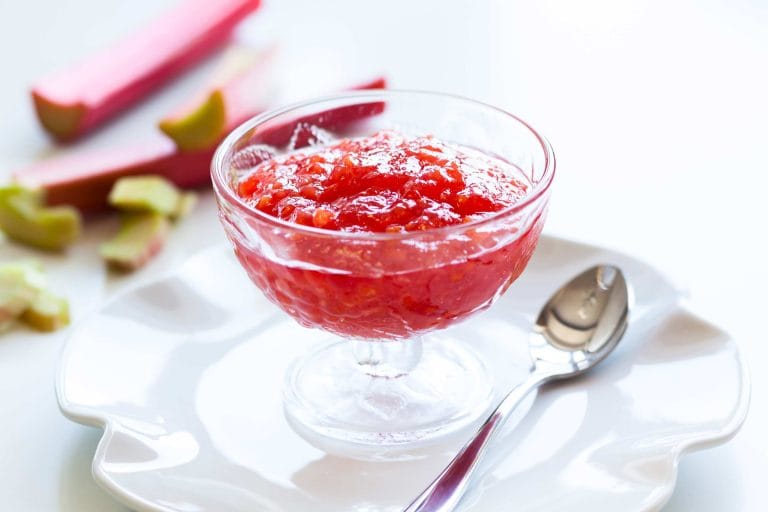 Compote de rhubarbe maison dans une coupe en verre et sur une assiette blanche avec quelques branches de rhubarbe à côté