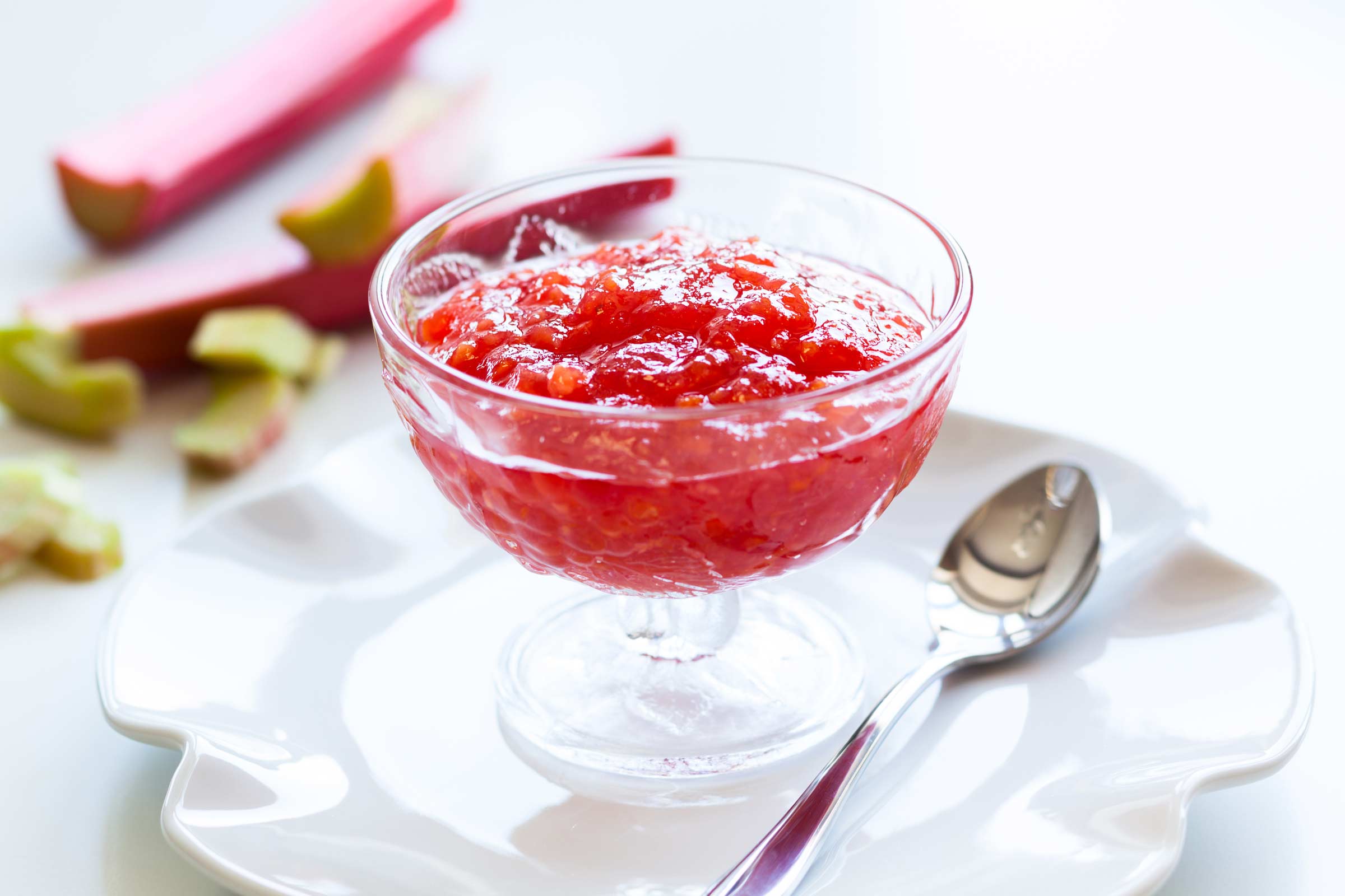 Compote de rhubarbe maison dans une coupe en verre et sur une assiette blanche avec quelques branches de rhubarbe à côté